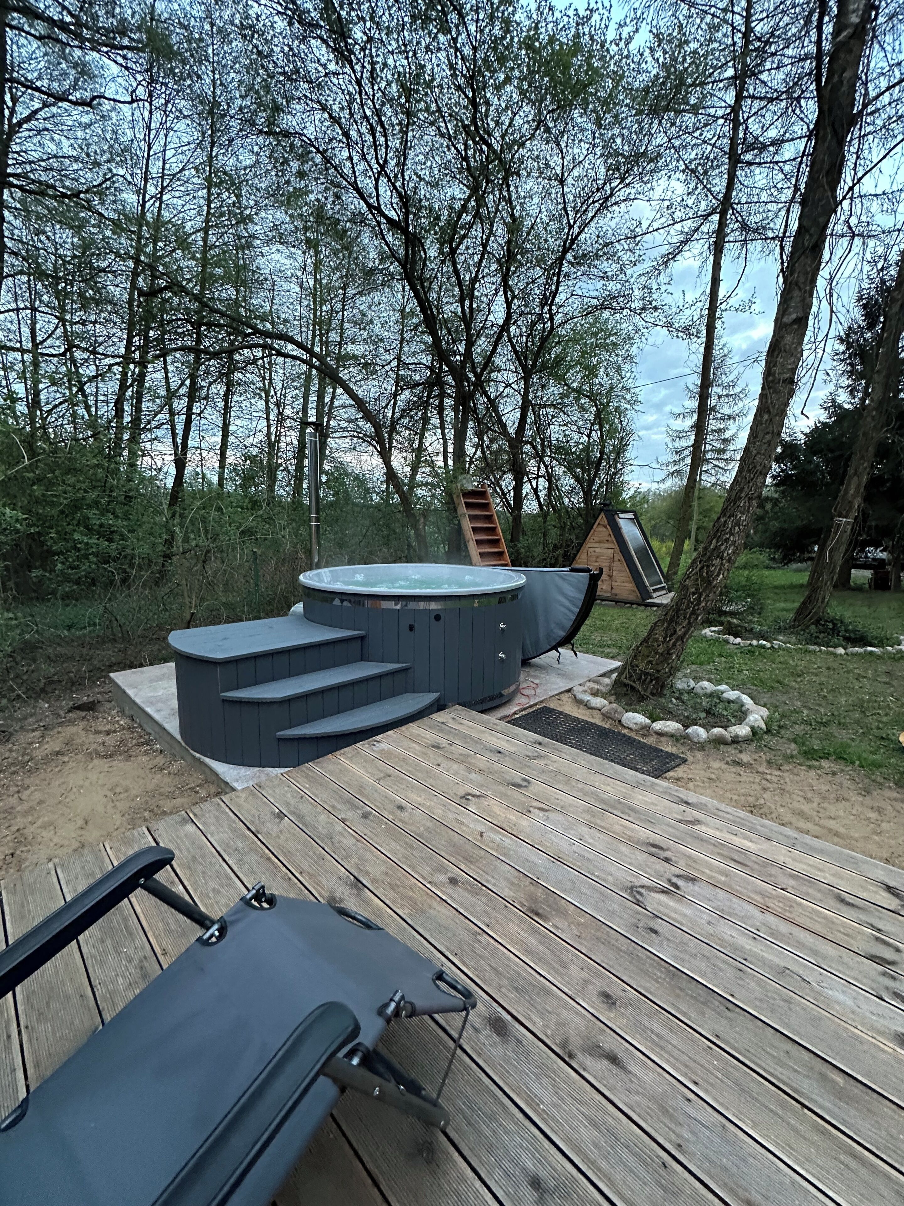 Un bain à remous avec des marches, entouré d’une terrasse en bois et d’arbres.
