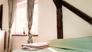 Une chambre à coucher avec un lit, des poutres en bois, une fenêtre avec des rideaux et une plante en pot posée sur le rebord de la fenêtre.