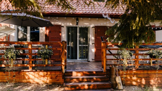 Une terrasse en bois avec des marches menant à une porte, entourée de plantes en pot et agrémentée d’un parasol.