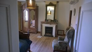 Una habitación con piso de madera, una chimenea, un espejo grande y un sillón estampado.