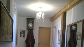 Un pasillo con suelo de madera, un candelabro y dos relojes en la pared.