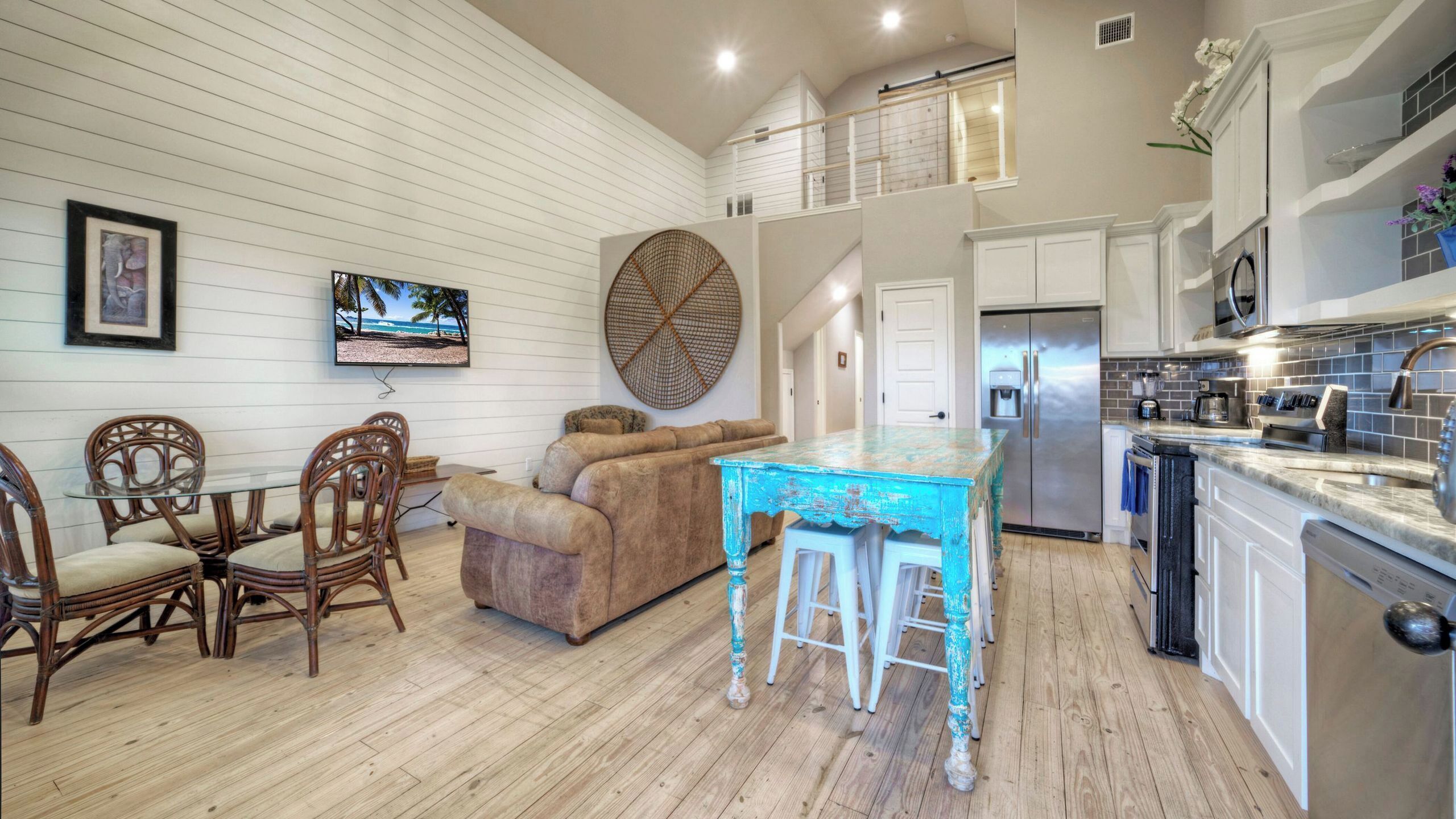 A spacious living area with a sofa, a dining table with chairs, a kitchen with a refrigerator, and a TV mounted on the wall.
