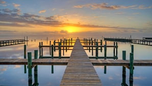A wooden pier extending into calm water with a sunset in the background. - Pool Access + Boat Dock Steps to the Gulf The Pintail by Avantstay (Corpus Christi)