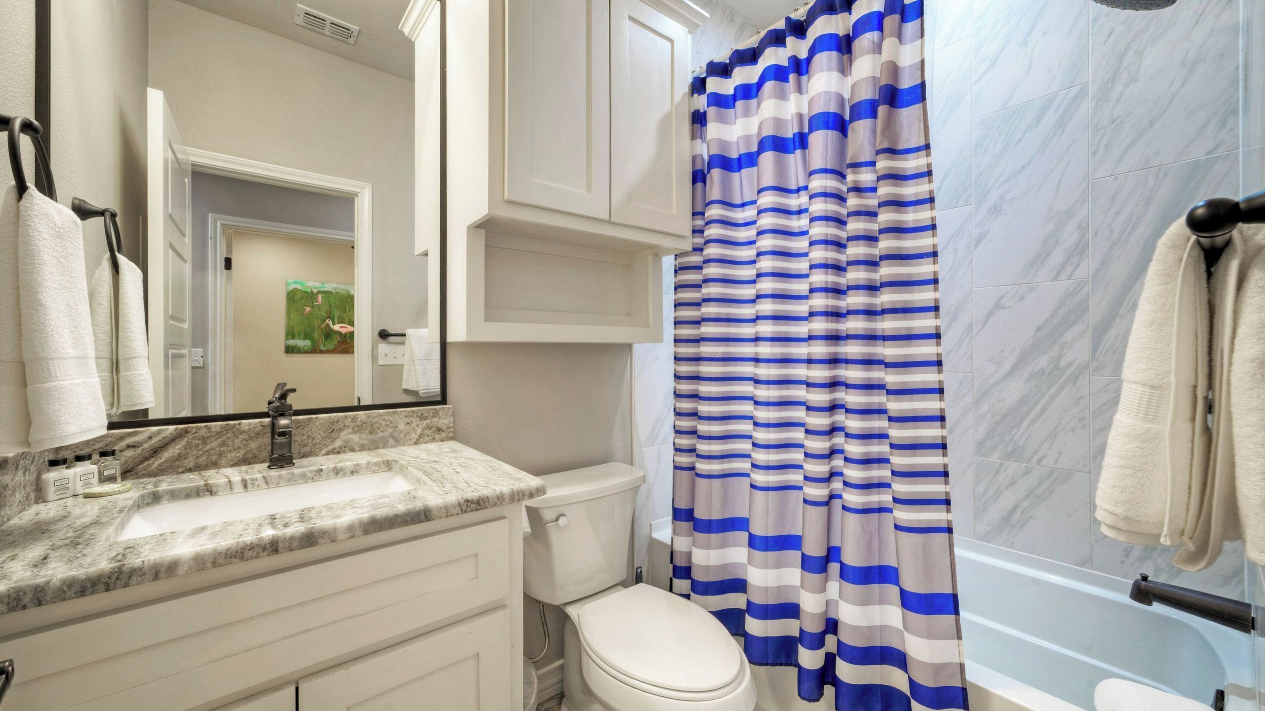 A bathroom with a marble sink, a toilet, a striped shower curtain, and a mirror.