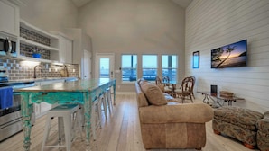 A spacious living area with a kitchen, a large window with a view, and a cozy seating arrangement. - Pool Access + Boat Dock Steps to the Gulf The Pintail by Avantstay (Corpus Christi)