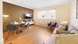 A modern living room with a dining area, wooden panel wall, flat-screen TV, and a large window. - NEW LISTING!!! Fantastic location for discovering London (London)