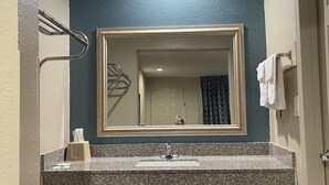 Un baño con lavamanos de encimera de granito, un espejo con marco dorado, un perchero y una puerta a la derecha.