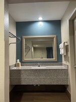 Un baño con lavamanos de encimera de granito, un espejo con marco dorado, un perchero y una puerta a la derecha.