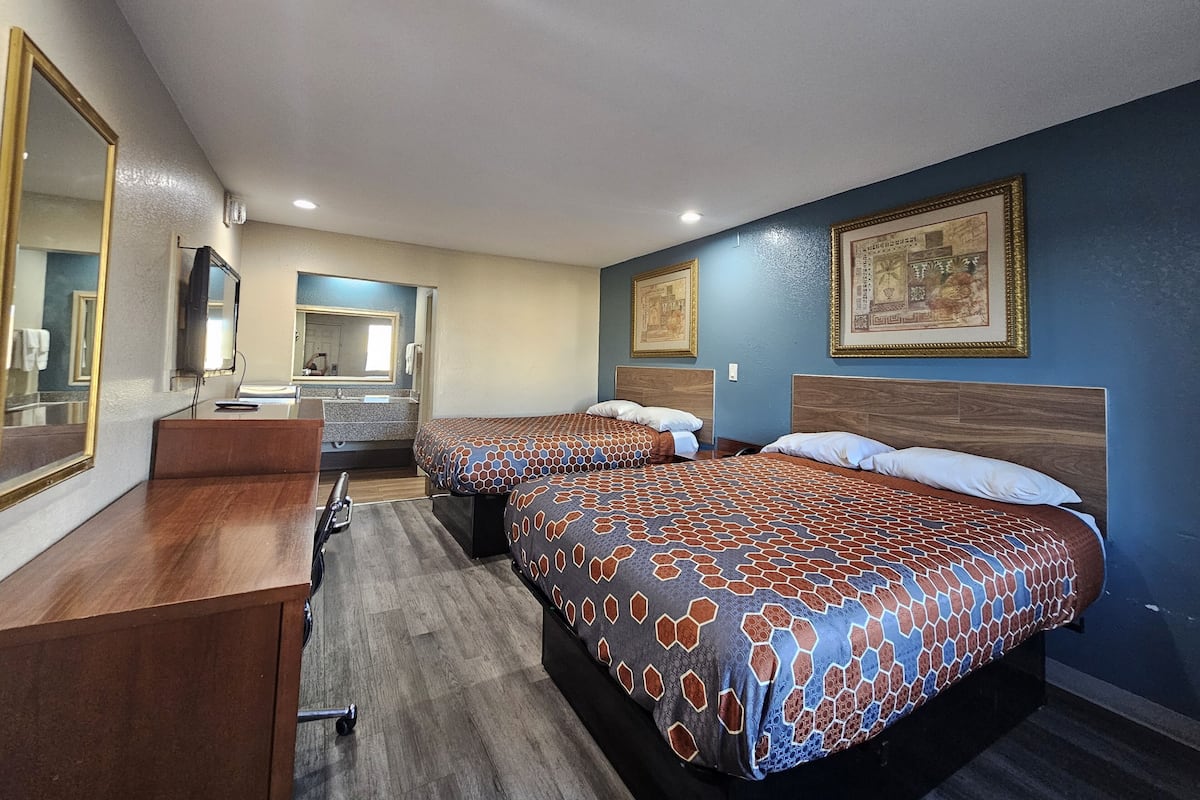 A hotel room with two beds, a desk, a mirror, and a bathroom visible in the background.
