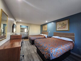 Habitación de hotel con dos camas, un escritorio, un espejo y un baño al fondo.