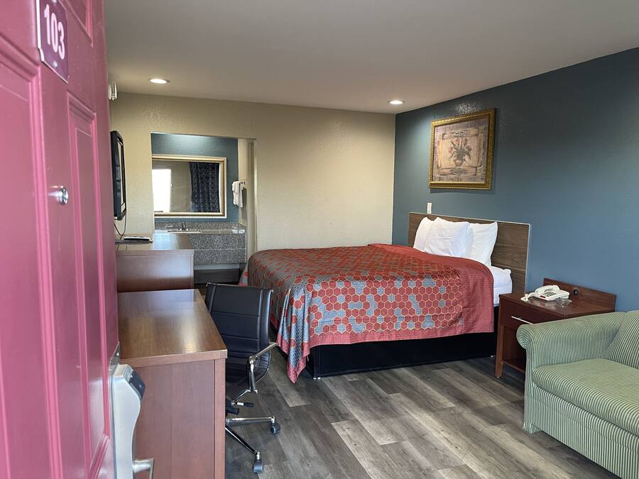 A hotel room with a bed, a desk, a chair, a nightstand, a phone, and a painting on the wall.