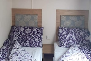 Due letti singoli con biancheria a motivi decorativi, testiere in legno e un piccolo comodino.