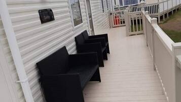 A covered outdoor area with a wooden deck, black outdoor furniture, and a white fence.