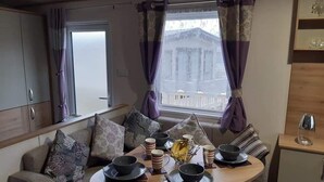 A cozy dining area with a round table set for four, surrounded by a sofa with patterned cushions. - Purple Palace, 3-bed Caravan, Ingoldmells (Skegness)