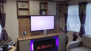 A living room with a flat-screen TV, a fireplace, and a sofa. - Purple Palace, 3-bed Caravan, Ingoldmells (Skegness)