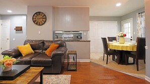 A living room with a brown leather sofa, a coffee table, and a dining area with a yellow tablecloth.