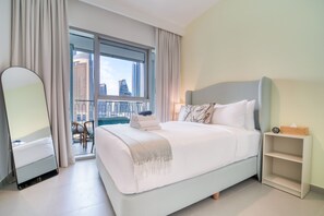 A modern hotel room with a large bed, a bedside table, a mirror, and a view of the city through large windows. - Burj Khalifa View | 2BR with Private Balcony (Downtown)