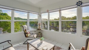 A sunroom with large windows, a table, a chair, and a view of a lake and trees. - Updated Branson Condo w/ Lake Taneycomo Views! (Branson)