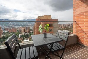 Enjoy the city view from this balcony with a table, chairs, and a potted plant.
