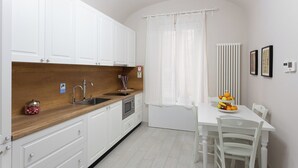 A kitchen with white cabinets, a wooden countertop, a sink, and a microwave. There is a dining table with chairs and a fruit bowl. - Colosseo House (Rome)