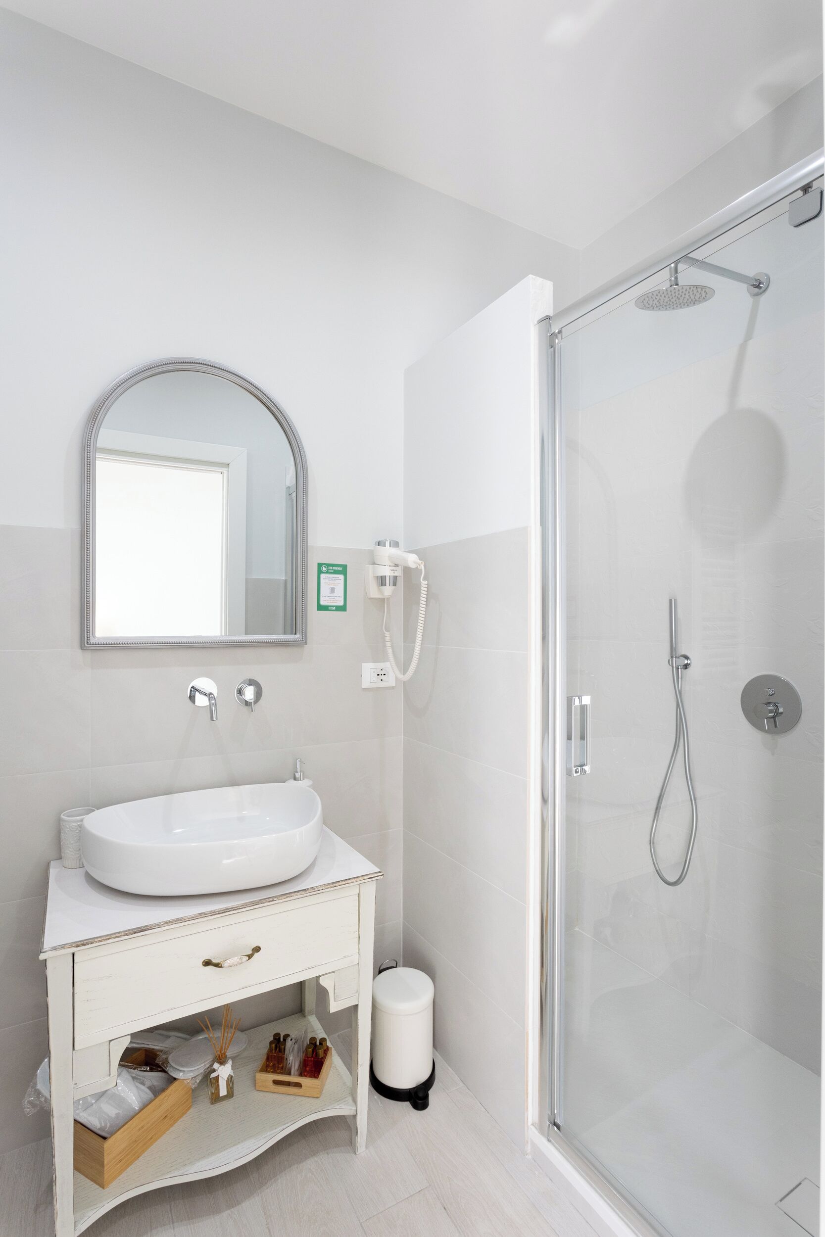 Un baño moderno con lavamanos blanco, espejo, cabina de ducha de vidrio y retrete.
