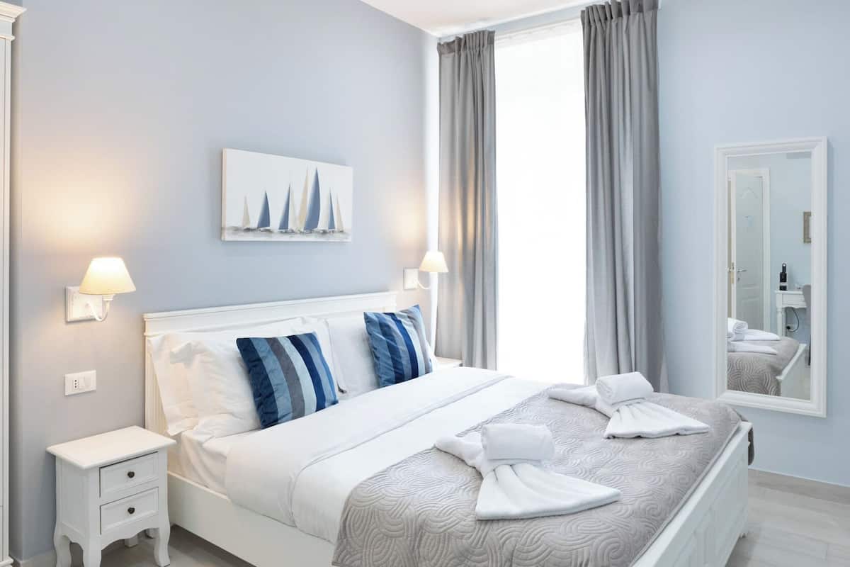 A modern bedroom with a large bed, bedside tables, a mirror, and a window with curtains.