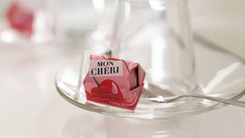 A clear glass wine glass on a reflective surface with a small packet of Mon Cheri chocolate.