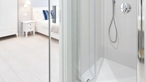 A modern bathroom with a glass-enclosed shower, a white vanity, and a bed in the adjacent room. - Colosseo House (Rome)