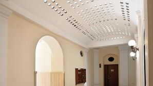 A spacious hallway with a patterned floor, a wooden door at the end, and a ceiling with circular cutouts. - Colosseo House (Rome)