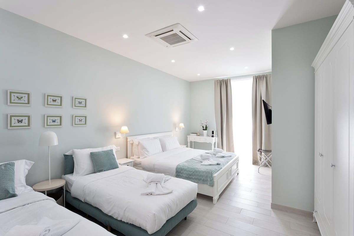 A hotel room with two beds, a bedside table with a lamp, a wardrobe, and a window with curtains.