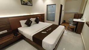 Une chambre d’hôtel avec un grand lit, une table de chevet avec un téléphone, une commode, une fenêtre avec des rideaux, une salle de bain avec un lavabo et un miroir, et un climatiseur fixé au mur.