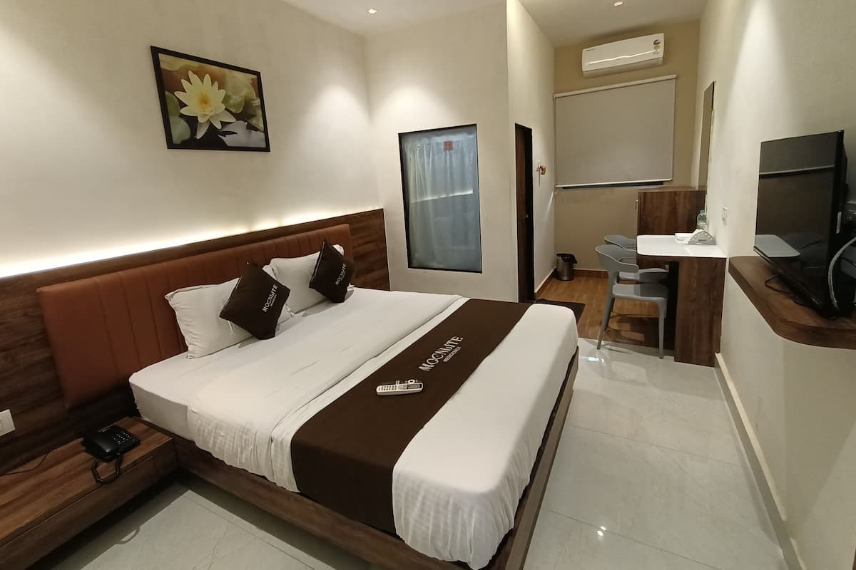 Una habitación de hotel moderna con una cama grande, una mesita de noche con teléfono, un escritorio con silla, un televisor y un equipo de aire acondicionado.