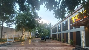 Une cour dallée avec un sol recouvert de carreaux décoratifs, une structure de jeu en métal avec des balançoires et un bâtiment doté de bandes lumineuses verticales et d’une enseigne dans une langue étrangère.