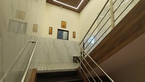 Un escalier aux murs de marbre et aux marches en bois, avec des rampes en métal et des œuvres d’art encadrées accrochées au mur.