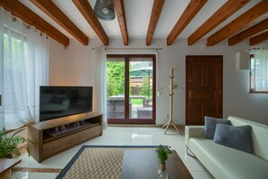 Un salón con televisor, vigas de madera, un sofá, una mesita de centro y vistas a un espacio exterior por una puerta de vidrio.