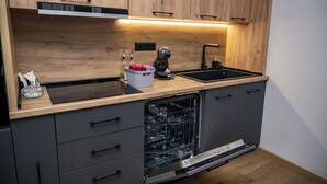 A modern kitchen with wooden cabinets, a built-in dishwasher, and a black countertop. - Luxury villa in the heart of Rila mountain. The only one 103 deg mineral spring (Sapareva banya)