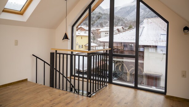 A spacious room with a high ceiling, a wooden staircase, and large windows offering a view of a snowy village. - Luxury villa in the heart of Rila mountain. The only one 103 deg mineral spring (Sapareva banya)