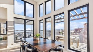 Una habitación amplia con una gran mesa de madera, varias sillas y ventanas grandes que ofrecen vistas a la ciudad.