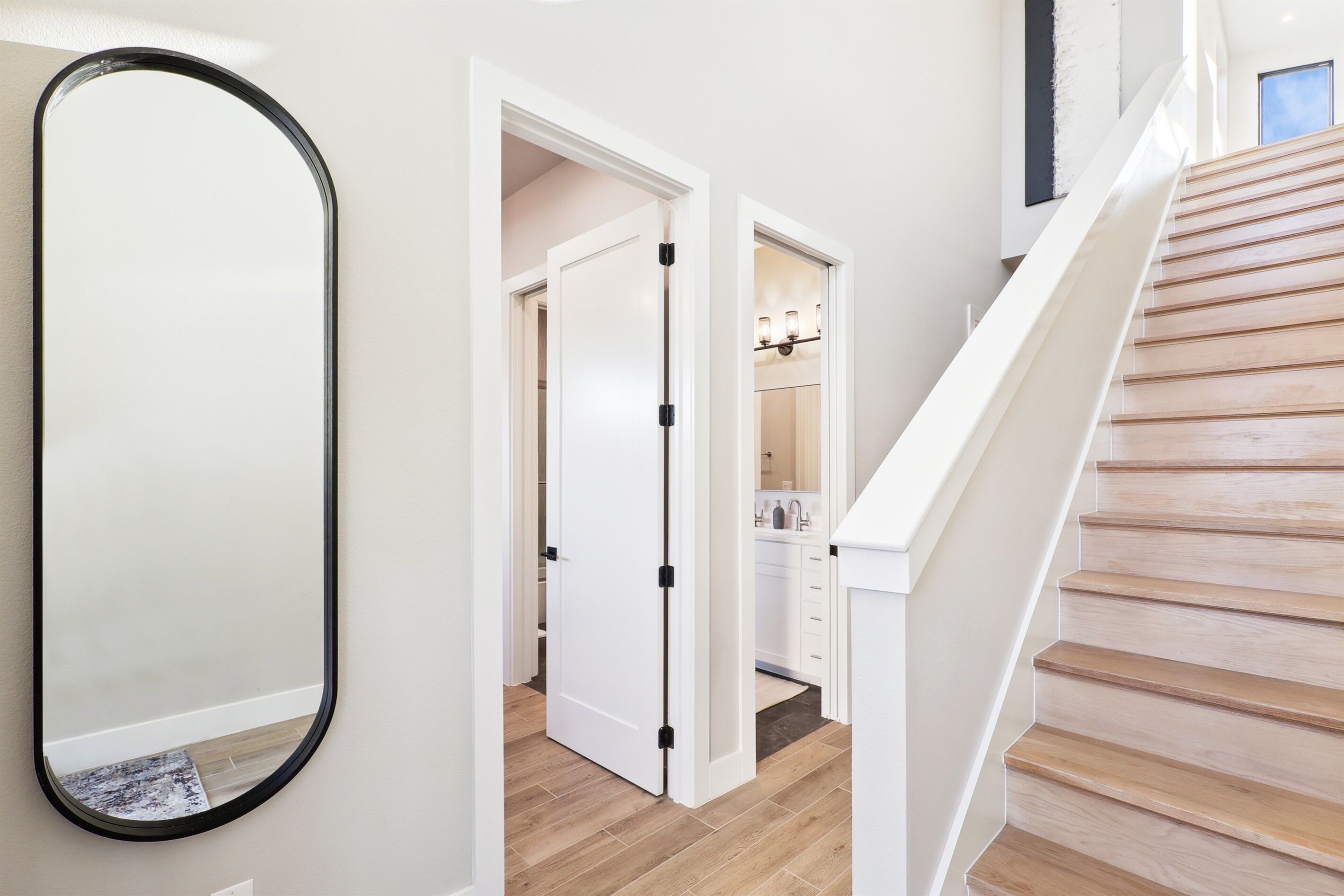 A hallway with a wooden staircase, a white door, and a mirror.