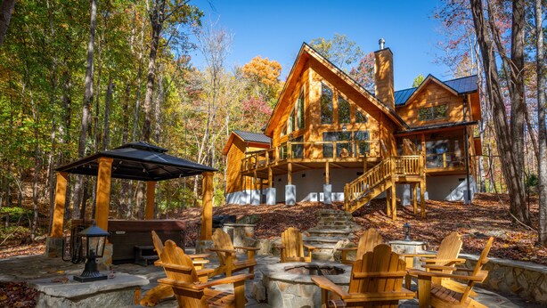 Une cabane dotée d’un foyer en pierre et de chaises en bois, entourée d’une forêt.