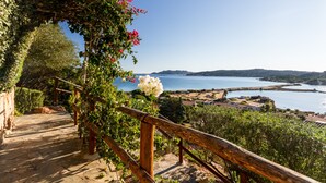 A stone staircase leading to a wooden railing overlooking a coastal landscape with a clear view of the sea and distant hills.