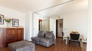 A living room with a grey sofa, ottoman, wooden cabinet, and a dining area with a table and chairs.