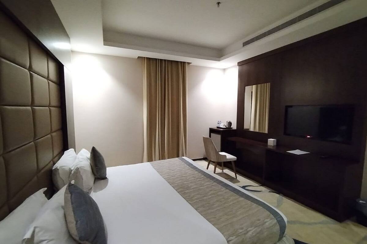A hotel room with a large bed, a desk, a chair, a television, and a window with curtains.