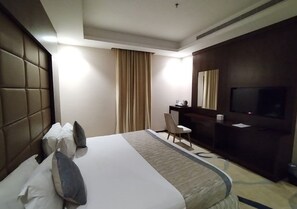 A hotel room with a large bed, a desk, a chair, a television, and a window with curtains. - Sansa Hotel (Jeddah)