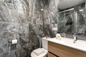 A bathroom with marble walls, a white toilet, a sink with a mirror, and a towel on the toilet seat. - Genteel Home Baños IV (Seville)