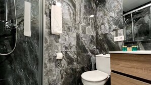 Een badkamer met een marmeren wand, een douchecabine van glas, een wit toilet en een houten wastafel met spiegel.