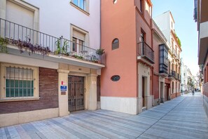 A narrow urban street lined with multi-story buildings, featuring balconies with plants and outdoor seating. - Genteel Home Baños IV (Seville)
