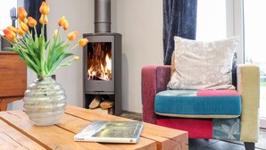 Ein gemütliches Wohnzimmer mit einem modernen Kamin, einem Holztisch mit einem Buch und einem bunten Sessel.
