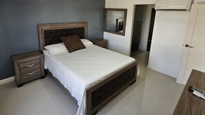 A bedroom with a bed, a nightstand, a dresser, a mirror, and a door. - Apartment Sleeps 6 With Pool Access (Portmore)