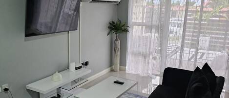 Un salon moderne doté d’un téléviseur à écran plat, d’un système de climatisation et d’une grande fenêtre agrémentée de rideaux légers.